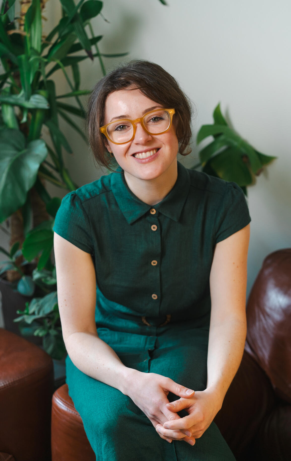 Photo of Ekaterina Photo of Ekaterina with a warm, welcoming smile, sitting on a counselling couch with lush plants in the background